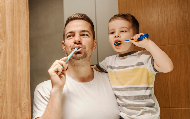 a father and son brush their teeth in the mirror