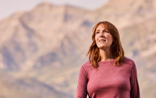 A woman smiles while standing in front of a mountain range