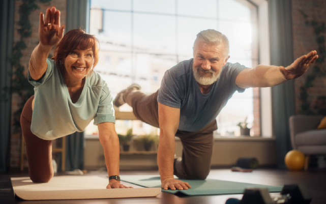 A woman and a man on the floor of their living room, holding a stretched yoga pose.